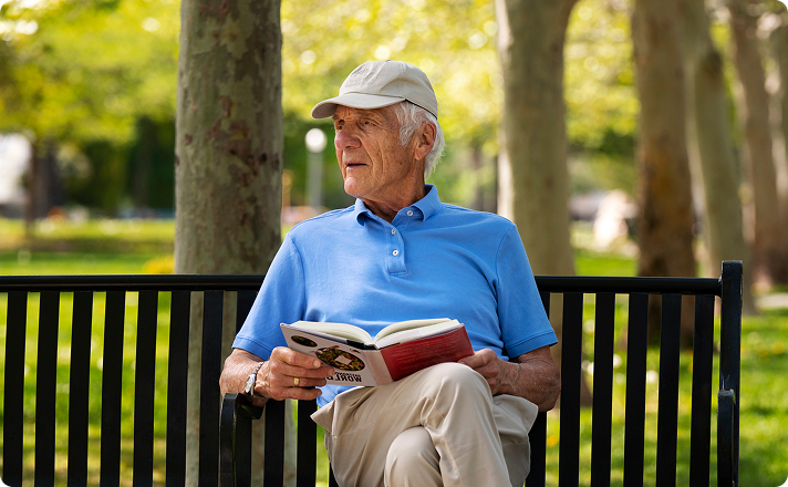 Older man in a cap reading a book on a park bench