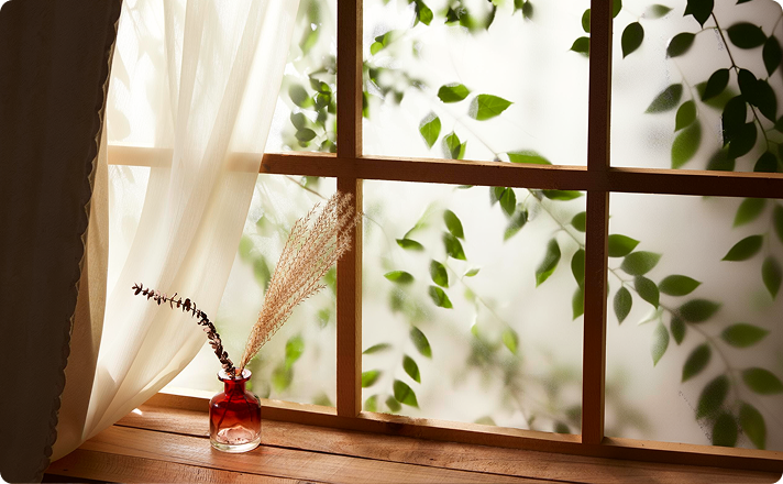 Window with sheer curtains and a small vase of dried grasses on the sill