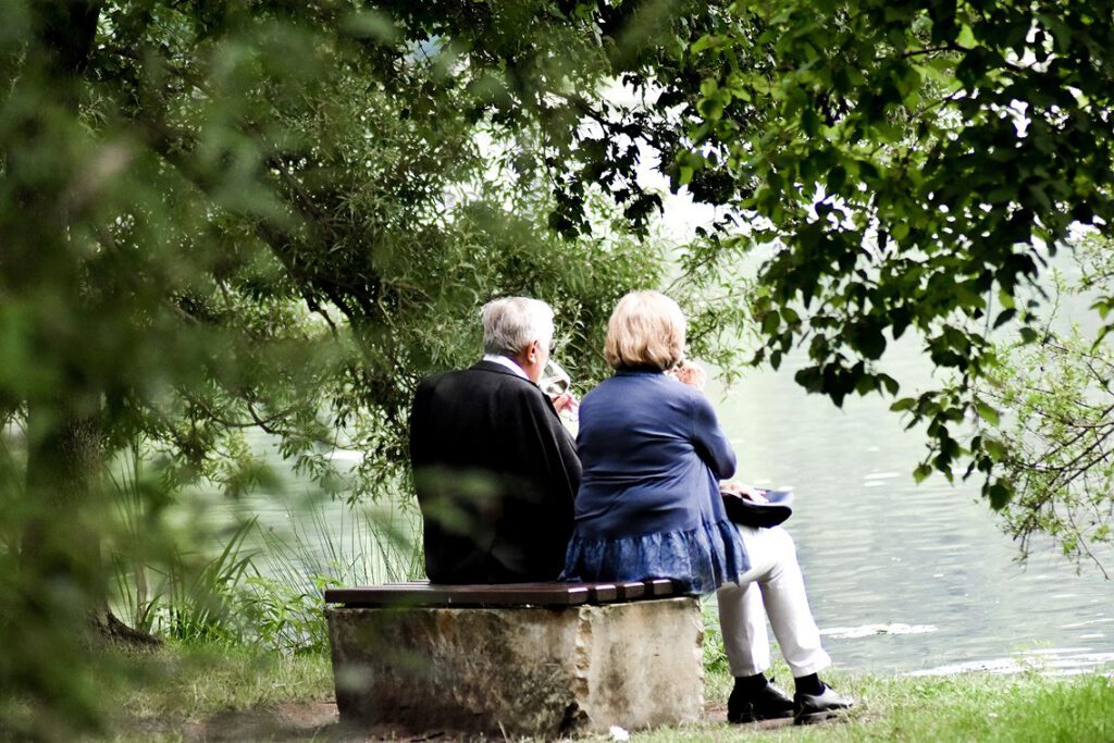 Older couple sitting together on a stone bench by a river