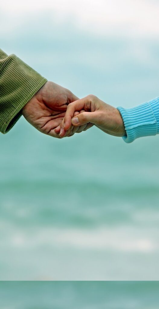 Two people holding hands with the sea behind them