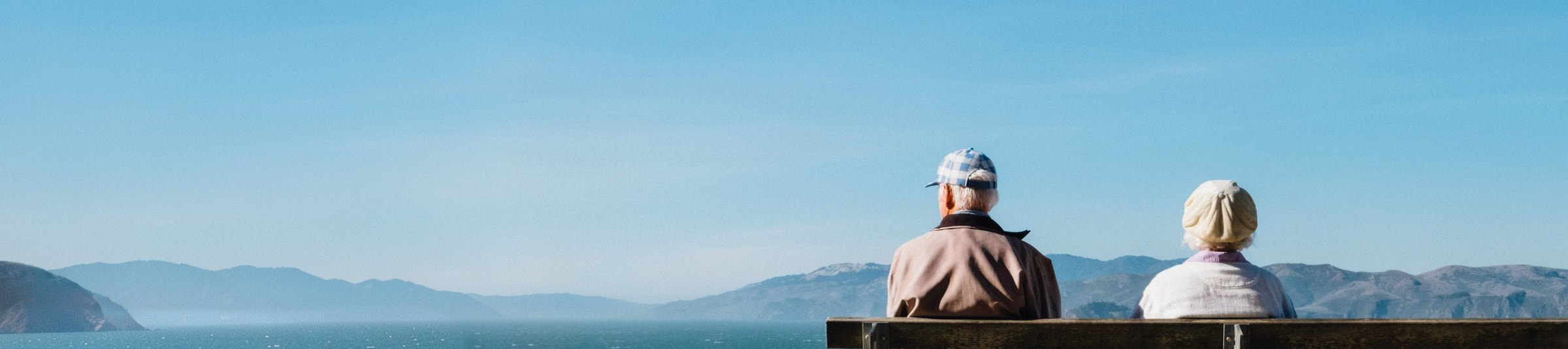 Older couple sitting on a bench looking out over a lake and mountains
